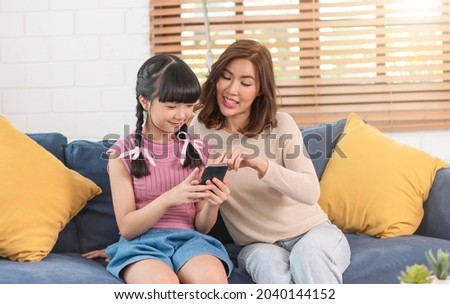 Happy Asian family using smartphone together on sofa at home living room.	
