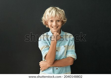 Happy cheerful smiling cute Caucasian schoolboy with arm on chest standing posing in classroom on chalkboard blackboard with numbers background. Elementary preteen school kid portrait.