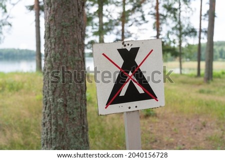 No camping sign in finland forest. White wooden sign with corssed out tent image. Camping is forbidden sign. Image taken in the woods near the lake or a river. Late summer colors - high resolution