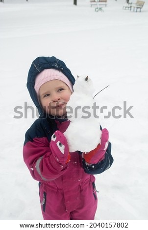a little girl with a snowman in her hands and snow on the floor joyfully screams for the New Year and Christmas.