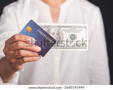 Hand of holding a mockup blue credit card and US dollar banknote while standing with a black background in the studio. Close-up photo. Money and business concept.