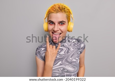 Crazy hipster rock fan shows horns gesture sticks out tongue enjoys listening favorite music wears wireless headphones on ears makes party wherever she is. Rock my soul. Youth lifestyle concept