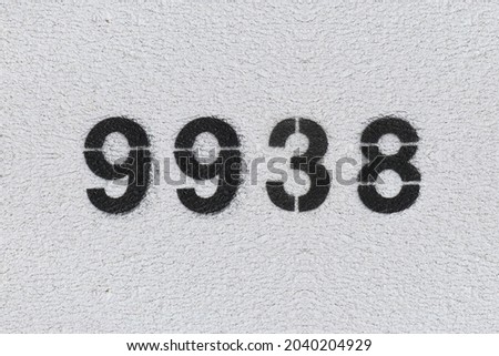 Black Number 9938 on the white wall. Spray paint. Number nine thousand nine hundred thirty eight.