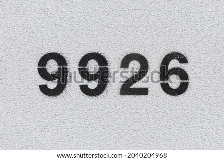 Black Number 9926 on the white wall. Spray paint. Number nine thousand nine hundred and twenty six.