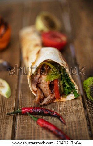 Shawarma sandwich fresh roll of lavash. Traditional Middle Eastern snack. On wooden background

