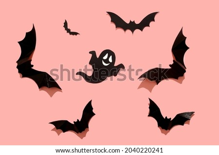 Black paper bat on a pink background. Close-up. Halloween concept. With a hard black shadow.