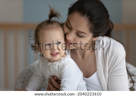 Happy sweet new mom cuddling cute baby, hugging, kissing little daughter girl. Young mother holding smiling toddler in arms with love, care, tenderness, enjoying motherhood, bonding with kid