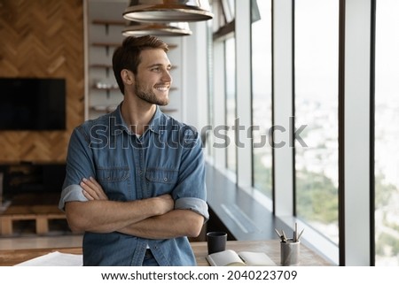 Smiling male employee stand at workplace look in window distance thinking pondering of future caress opportunities perspectives. Happy man imagine visualize success. Business vision concept.
