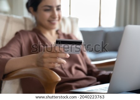 Ecommerce client. Young mixed race woman web shop customer using bank card to make safe secure electronic payment online via app on pc. Focus on credit card and laptop computer used by ethnic female