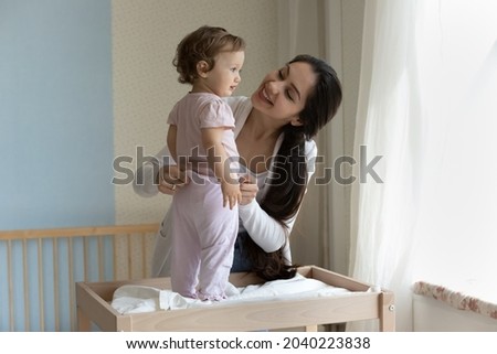 Happy young mom dressing cute toddler girl on baby changing table. Loving mother talking and caring of little child with tenderness, affection, enjoying motherhood, maternity leave. Childcare concept Royalty-Free Stock Photo #2040223838