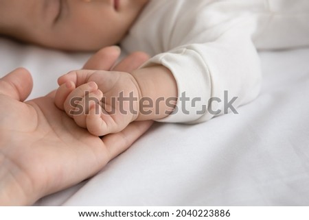 New mom and newborn baby hands close up. Mother holding arm of few month infant son or daughter sleeping on white sheet, touching kid with love and tenderness. Childbirth, motherhood concept. Close up Royalty-Free Stock Photo #2040223886