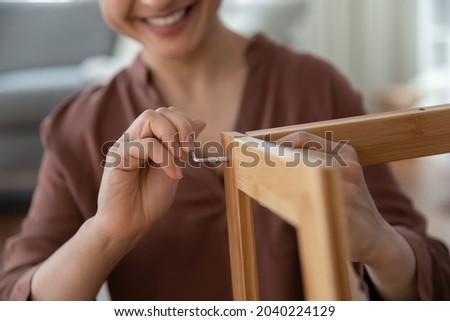 Do it yourself. Close up shot of smiling young female assembling flat pack furniture at home using hex key. Satisfied woman customer screw details of wooden shelf together with allen key by own hands Royalty-Free Stock Photo #2040224129