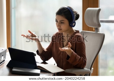 Online briefing. Hindu female office worker in headset use tablet pc take part in virtual conference from workplace. Young indian woman contact colleague by video call speak talk to boss discuss idea