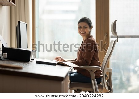 Modern day worker. Portrait of happy biracial business woman freelancer sit by computer at comfy workplace at corporate workspace or at home. Smiling young indian lady office employee look at camera Royalty-Free Stock Photo #2040224282