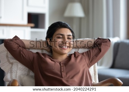 Chilling at home. Tranquil young indian female sit on comfy chair enjoy calm peaceful rest at living room hold hands over head. Lazy serene ethnic lady meditate breath fresh air relax with closed eyes Royalty-Free Stock Photo #2040224291