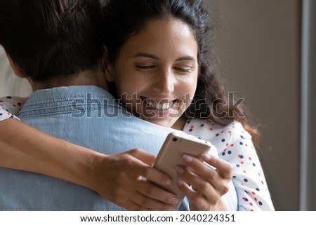 Smiling cheater woman holding smartphone using e-date application while hugging husband, back view, close up. Split in family, relationship problem and crisis, social media dependence, treason concept Royalty-Free Stock Photo #2040224351