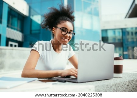 Successful Black Student Girl Using Laptop Computer Learning Online Watching Educational Webinar And Doing Homework Sitting Outdoor Near Urban University Building. Education And Studentship Royalty-Free Stock Photo #2040225308