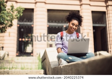 Cheerful Black Student Girl Sitting With Laptop Learning Online And Communicating Remotely During Educational Virtual Lecture Outdoors. Modern Study And Education, E-Learning Royalty-Free Stock Photo #2040225374