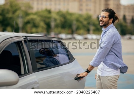 Cheerful middle-eastern young man in casual getting in taxi, open auto back door, taking cab home or to business meeting, looking at copy space. Car service, transportation, taxi concept Royalty-Free Stock Photo #2040225407