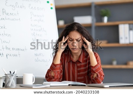 Tired From Work. Portrait of exhausted stressed young woman suffering from headache, touching and massaging her forehead and temples, sitting at desk near whiteboard, thinking about problems Royalty-Free Stock Photo #2040233108
