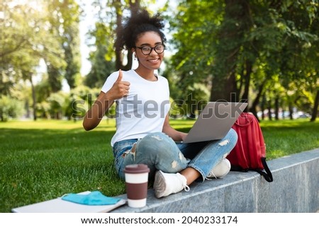 African Student Girl Gesturing Like Posing With Laptop Approving Educational Online Program Or Website Showing Thumbs Up Gesture And Smiling To Camera Outdoor. College Learner Likes E-Learning Royalty-Free Stock Photo #2040233174