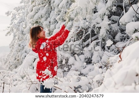 Woman in red jacket among snowy trees in winter forest. Traveller woman with snow trees in December sunny day