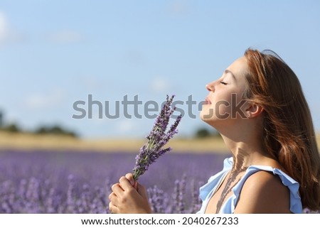 Side view portrait of a happy woman smelling lavender flowers bouquet in a field Royalty-Free Stock Photo #2040267233