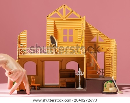 A toy house and a hand depicts a little man. A happy buyer of his own house, his own home, a funny concept. dollhouse on a pink background, toy furniture inside.