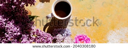 Frame of blooming lilacs on a yellow concrete background, cup of coffee, top view. white coffee cup, blooming branches of purple lilac on table. Copy space