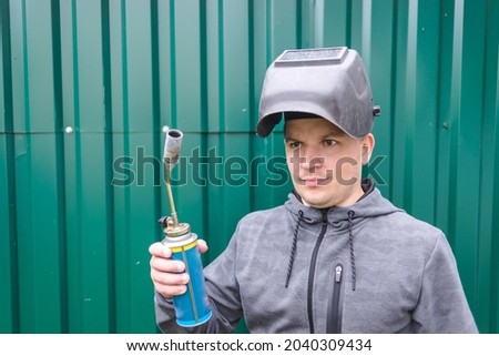 Man with a welder mask holds a gas burner in his hand