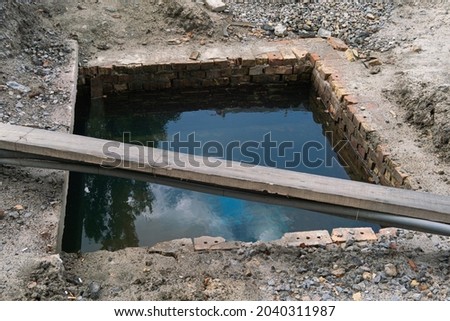 Water pipe repair in the city on the road, clouds and trees are reflected on the water surface in the well