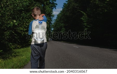 A small boy carries a large bottle of clean water along the road