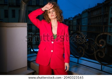 A woman of Caucasian appearance with in a bright red suit posing in the evening on a city street, fashionable photo shooting