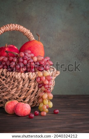 Fresh ripe fruits in wicker basket. Apples, grape, pear in basket at the wooden table