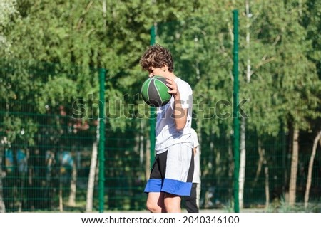 Cute teenager plays basketball at city playground. A boy holds basketball ball in his hands outside. Active life, hobby, sports for children	