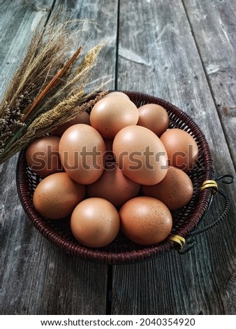 Eggs. A group of fresh chicken eggs in brown rattan basket. On rustic wooden table Background with dried grass. Still Life. Protein. Raw food. Ingredient. Close view and Selective Focus. Telur.