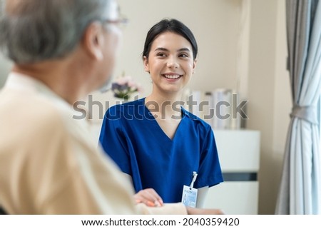 Asian nurse take care of senior man on wheelchair at nursing home care. Attractive happy Caregiver girl doctor greeting and talking with older elderly mature disabled patient male in hospital ward.