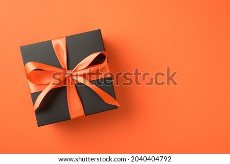 Top view photo of black giftbox with orange satin ribbon bow on isolated orange background with empty space Royalty-Free Stock Photo #2040404792