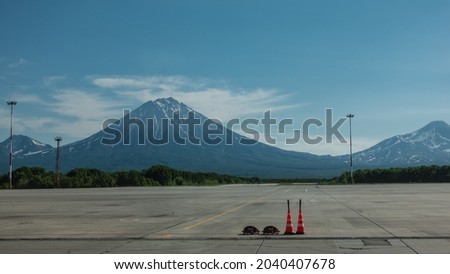 There is a marking on the runway of the airfield. Majestic conical volcanoes with snow-covered slopes rise against the blue sky. Petropavlovsk-Kamchatsky.  Royalty-Free Stock Photo #2040407678