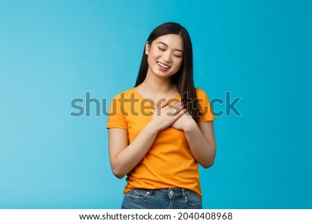 Lovely asian woman with dark haircut close eyes press hands heart gently smiling, tilt head cute cherish heartwarming memories, daydreaming, imaging beautiful dream, stand blue background Royalty-Free Stock Photo #2040408968
