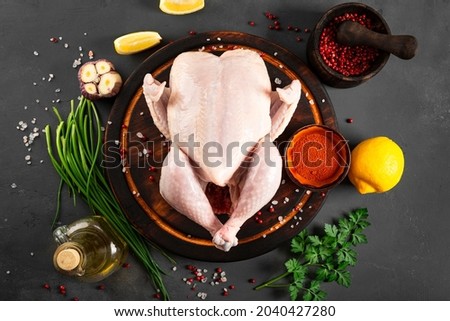 Whole raw chicken on the wooden cutting board and seasonings for cooking it top view, free space for text. Dark gray background. High quality photo