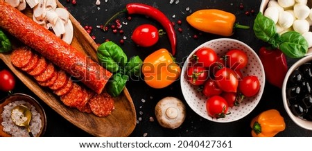 Web banner with pizza ingredients on the dark gray background. Pepperoni sausage, mozzarella cheese, tomatoes, olives, mushrooms and flour are different products for making pizza and pasta