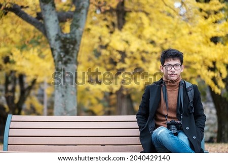 Happy man enjoy at the park outdoor in Autumn season, Asian traveler in coat and camera against Yellow Ginkgo Leaves background