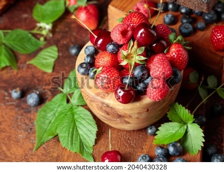 Assorted fresh berries with leaves. Strawberries, raspberries blueberries, and sweet cherries on an old vintage table. 