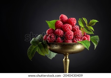Fresh raspberries with leaves in an old brass dish on a black background.