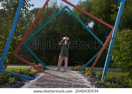 The girl holds virtual reality glasses on her head with her hands, stands against the background of iron arched pipes. The concept of the future. High quality photo