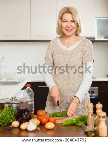 Mature housewife cooking with veggy lunch in kitchen