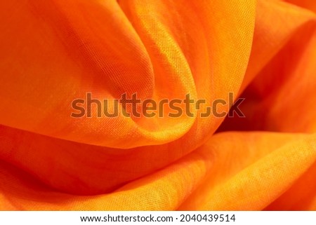 Background from material of yellow-orange color. Fabric with pleats and waves. Light orange tint pattern