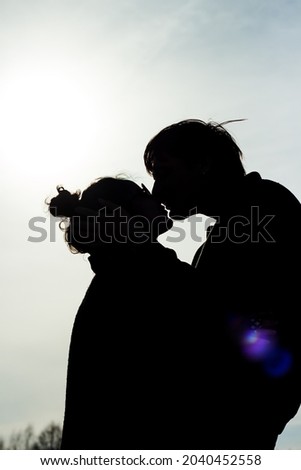 happy couple kissing silhouetted on blue sky background copy space text. Two lovers man woman embracing outdoors backlit by spring summer sun. love emotion relations