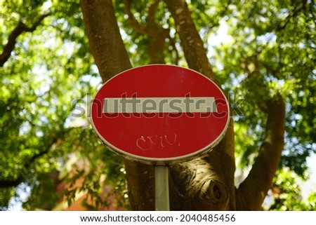 A closeup shot of a red no entry sign with a white horizontal line in front of a tree in a park